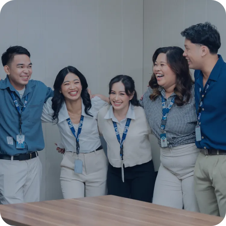 Five colleagues smiling and embracing in an office setting.