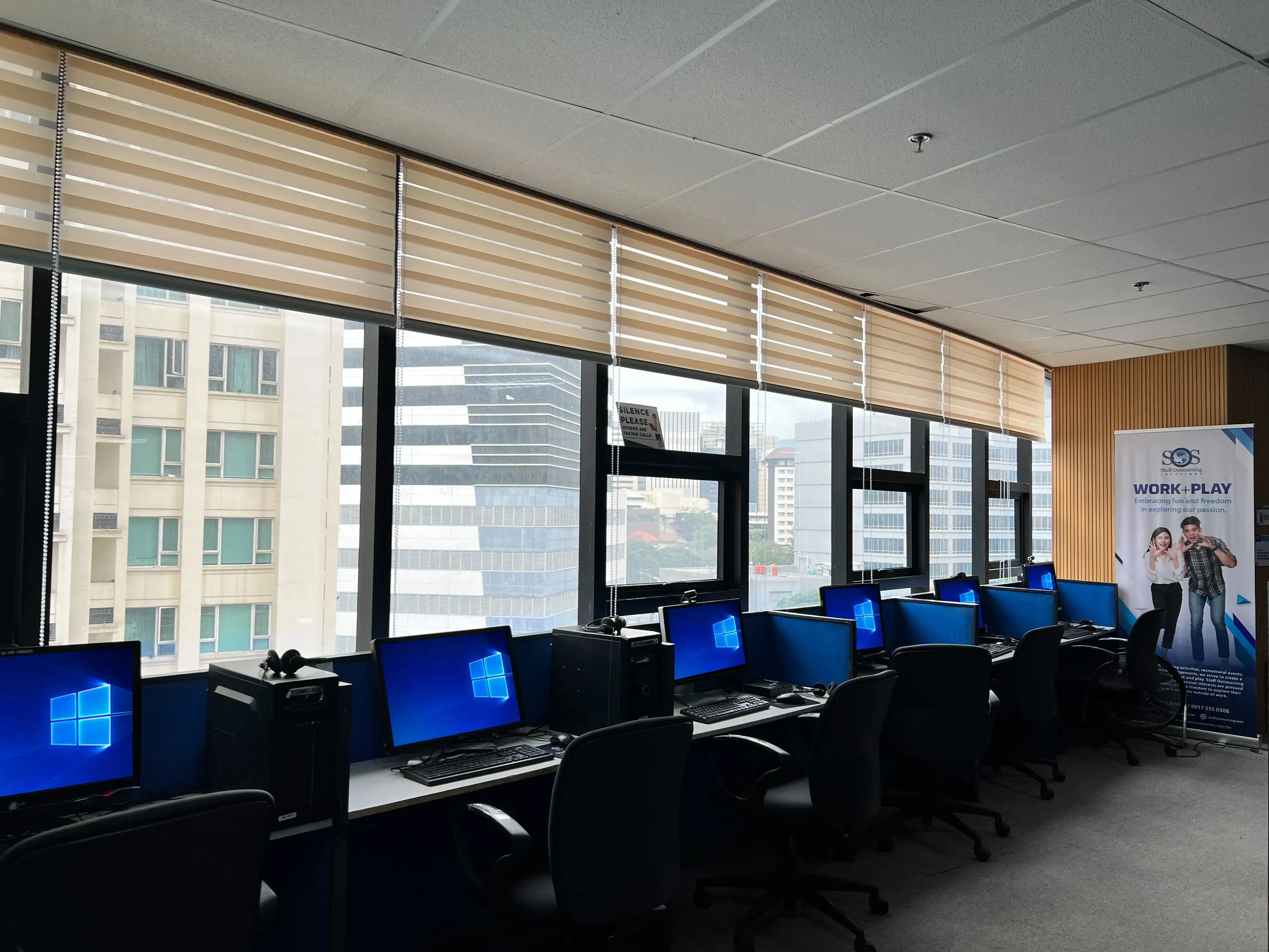 Rows of computers in a modern office with large windows.