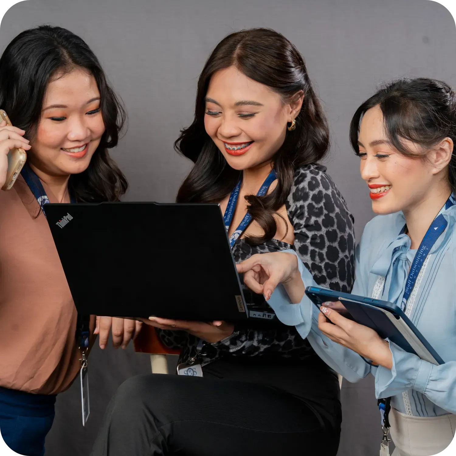 Three women smiling and collaborating on a laptop.