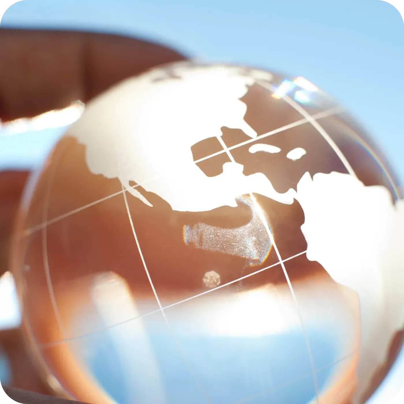 Glass globe with map of North America, held by a hand, against a blue sky.